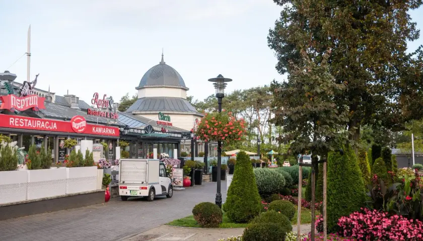 Spacer po alei gwiazd w Międzyzdrojach, z restauracjami i kawiarniami po lewej stronie, a zielenią i drzewami po prawej.