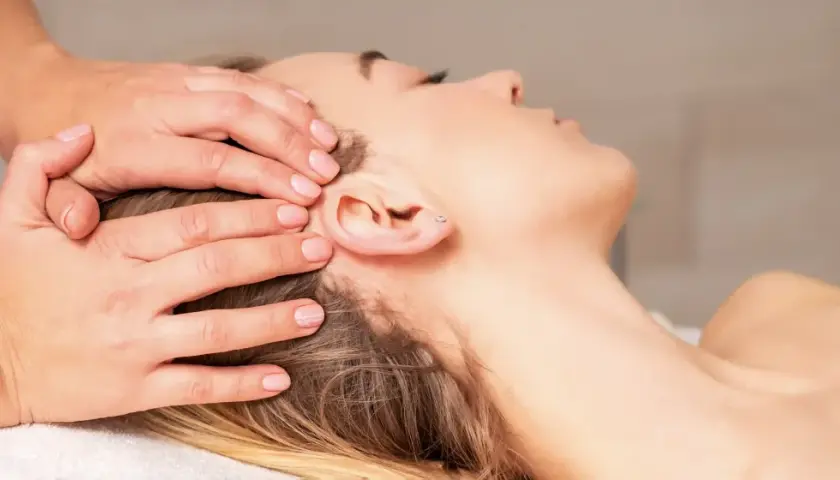 Mains douces appliquant une thérapie cranio sacrée sur la tête d'une femme détendue.