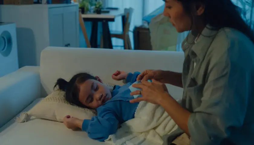 Mamma accarezza dolcemente il suo bambino che dorme sul divano, uno dei tanti bambini che si svegliano di notte.