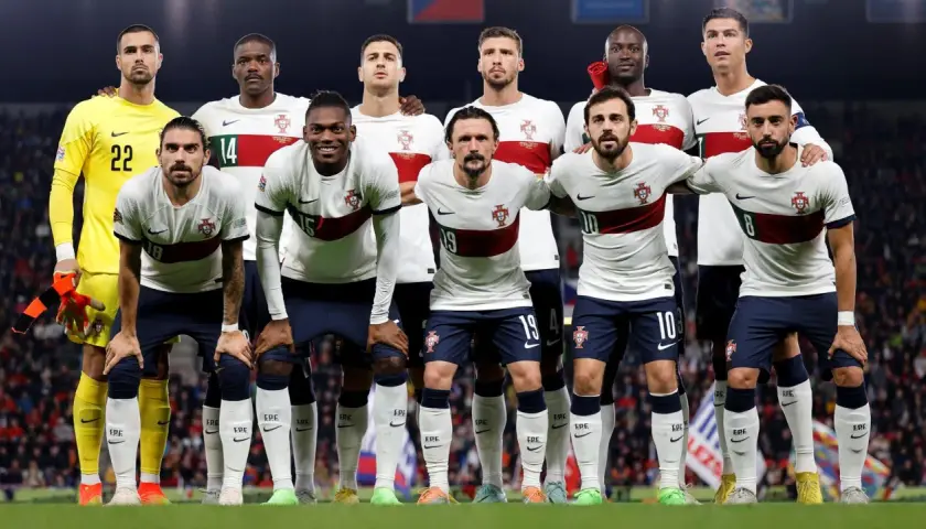 Drużyna piłkarzy Portugalii w białych strojach z czerwonym pasem, gotowa do meczu.