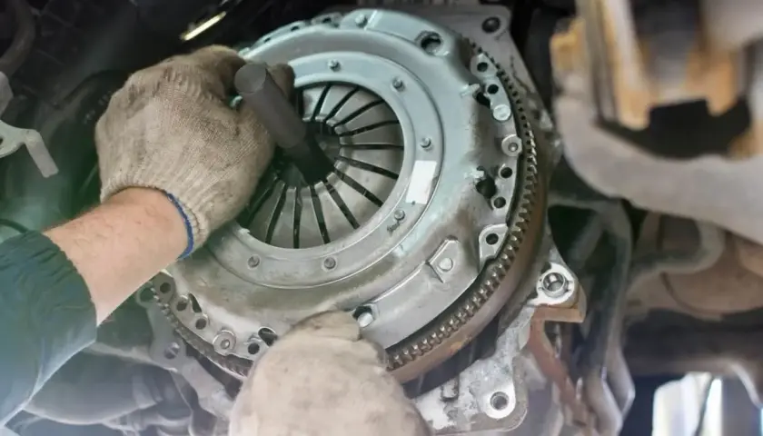 Mechanik w rękawiczkach naprawia sprzęgło samochodowe.
