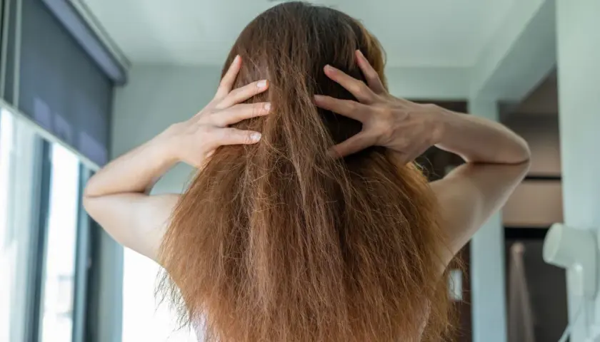 Manos revolviendo el pelo encrespado de una mujer, mostrando la textura seca y desordenada.