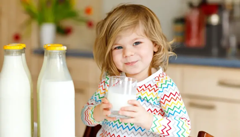 Bambina sorridente con bicchiere di latte vaccino cos'è. Due bottiglie di latte fresco sul tavolo.
