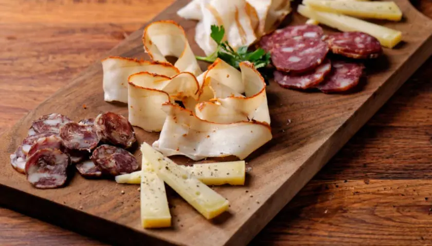 Un invitante tagliere di antipasti con salumi affettati, formaggio e lardo su un tagliere di legno rustico.
