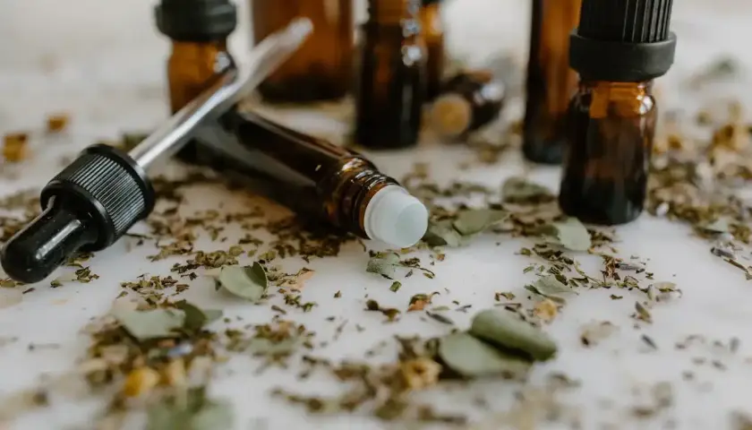 Butelki z ciemnego szkła, pipeta i rollerball otoczone suszonymi ziołami. To może być zestaw do tworzenia własnych olejków, które można aplikować jak vaporisateur spray.