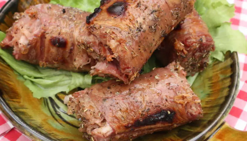 Trois andouillettes grillées au barbecue, servies sur un lit de laitue dans une assiette décorative.