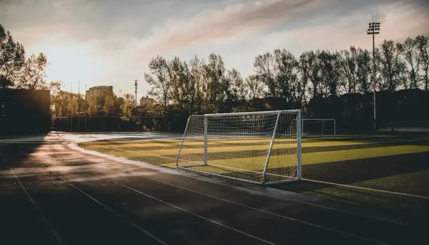 Piłkarskie boisko o zachodzie słońca. Bramka czeka na zawodników, a bieżnia jest pusta. Var.