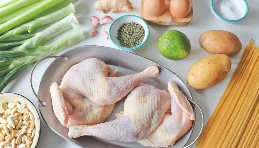 Ingredientes para un reconfortante caldo de gallina: pollo crudo, apio, cebolla, ajo, jengibre, papas, lima, especias, sal y pasta.