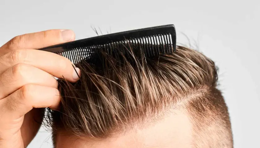 Hombre peinando su cabello, buscando recuperar pelo entradas naturalmente.