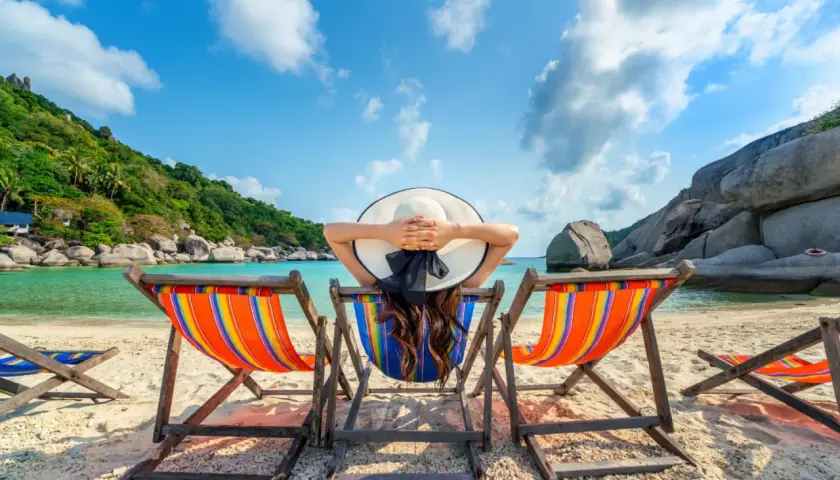 Kobieta w kapeluszu odpoczywa na leżaku na tropikalnej plaży.