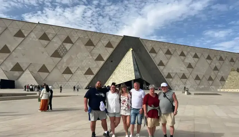 Rodzina pozuje przed nowoczesnym, geometrycznym budynkiem – nowym muzeum w Egipcie.