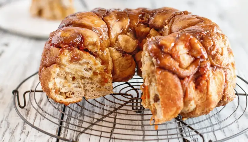 Pyszny, karmelizowany monkey bread przepis na okrągłej kratce. Ciasto jest lekko rozwarstwione, z widocznymi kawałkami ciasta.