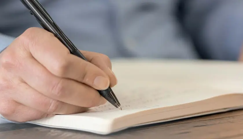 Hand schreibt mit einem Stift in ein Notizbuch. Wichtige Details für das protokoll schreiben festhalten.