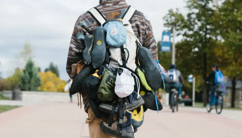 A climber's backpack is laden with multiple pairs of climbing shoes, a testament to a day of ascents.