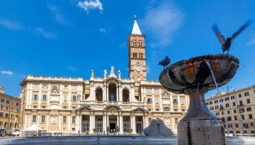 La basilique Sainte-Marie-Majeure se dresse fièrement sous un ciel bleu, avec une fontaine et des pigeons au premier plan.