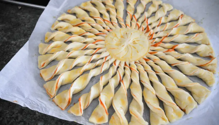 Tarte soleil prête à cuire, avec sa pâte feuilletée torsadée et son centre décoré. Un délice visuel et gustatif.