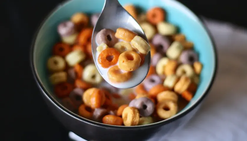 Kolorowe kółeczka płatków śniadaniowych w mleku, nabierane łyżką. Pyszny, kolorowy cereal po polsku na śniadanie.