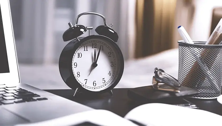 Budzik pokazuje 12:00. Ile minut trwa rozprawa w sądzie? Czas biegnie, a na biurku leżą dokumenty i długopisy.
