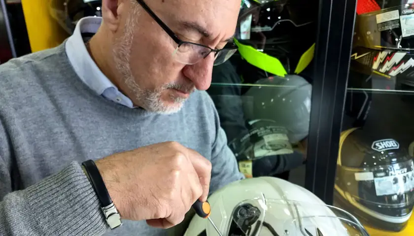 Uomo con cacciavite regola la visiera di un casco bianco, assicurandosi che il casco debba avere la visiera priva di graffi.