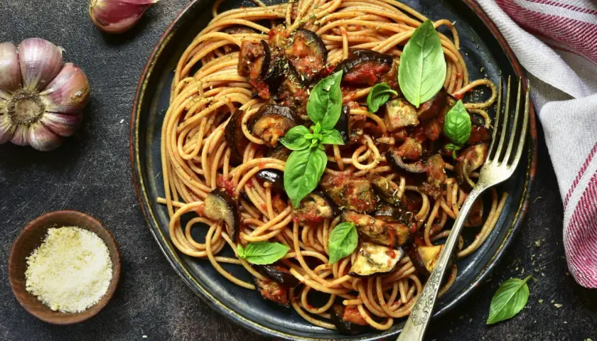 Assiette de pâtes à l'italienne, spaghetti avec aubergines et sauce tomate, garnie de basilic frais. Ail et parmesan à côté.