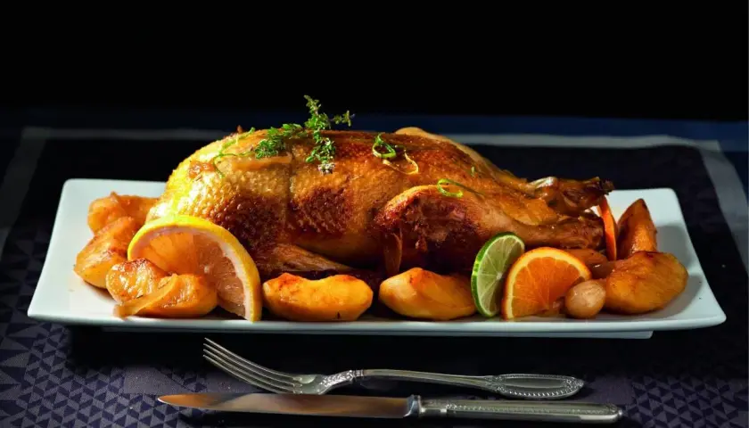 Canard rôti, pommes caramélisées et agrumes en accompagnement. Une canette dorée, prête à être dégustée.