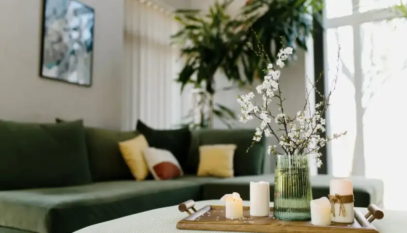 Stolik z świecami i gałązką kwitnącej wiśni, zielona kanapa w tle. Aranżacja zgodna z zasadami feng shui, wprowadzająca harmonię.
