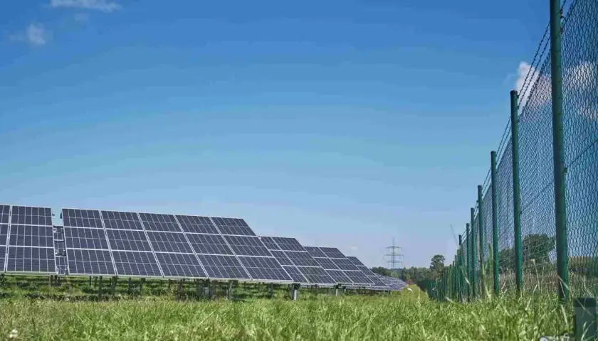 Panele słoneczne na zielonej łące, w tle niebieskie niebo. Trwa budowa falownika, który zamieni energię słoneczną na prąd.