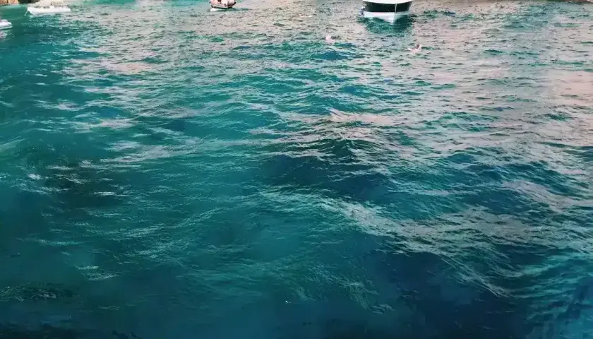 Acqua cristallina e turchese vicino all'ingresso di una grotta, con barche e bagnanti che godono della bellezza della Grotta Azzurra.