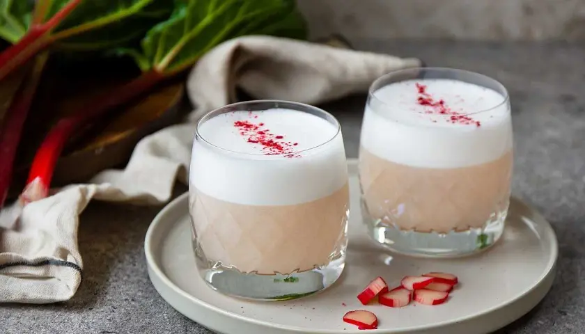 Två glas med en krämig rabarber sour, toppad med skum och strödd med torkad rabarber.