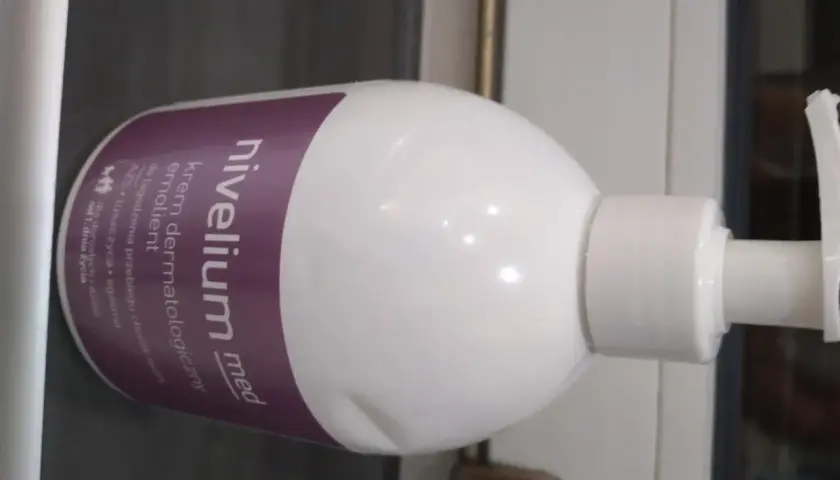 Biała butelka z pompką, na której widnieje napis "nivelium med krem dermatologiczny".