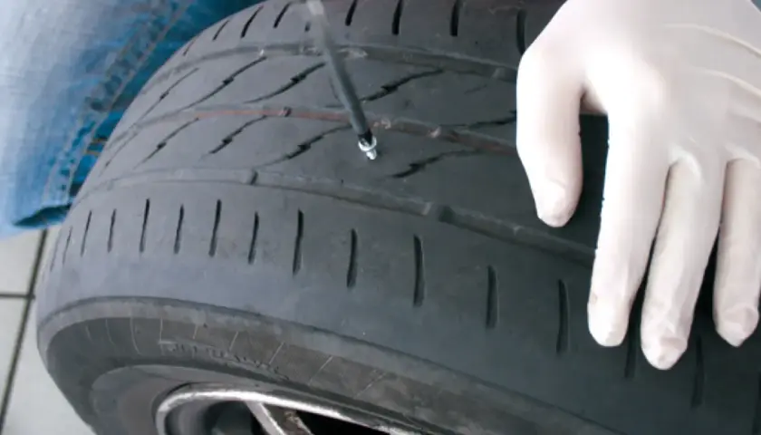 Mano enguantada inserta herramienta para reparar pinchazo. Es seguro reparar un pinchazo si se hace correctamente.