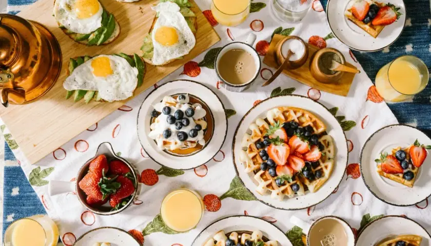 Un festin de brunch : toasts à l'avocat et œuf au plat, gaufres aux fruits rouges et myrtilles, jus d'orange et café.