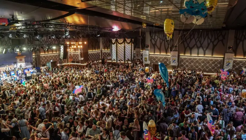Volles Festzelt beim Starkbierfest Nockherberg. Menschen in Tracht feiern ausgelassen, mit Bierkrügen in den Händen und bunten Ballons über ihnen.
