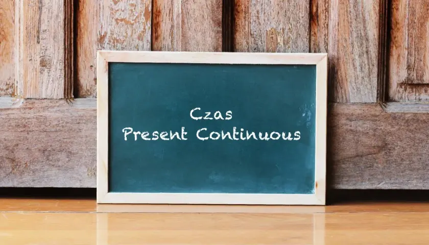 Tablica z napisem "Czas Present Continuous" na tle drewnianych drzwi. Uczysz się, co to jest present continuous?