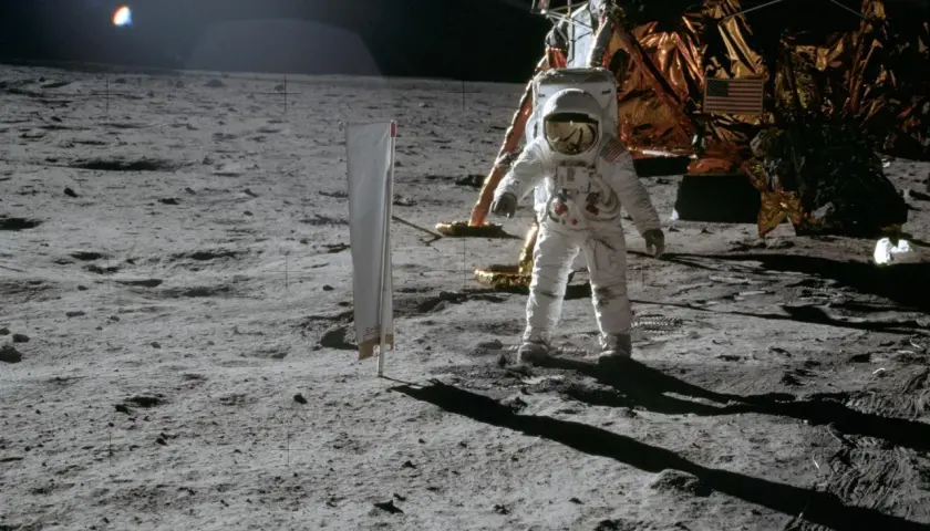 Astronaut na Księżycu podczas misji Apollo, obok lądownika. W tle amerykańska flaga.