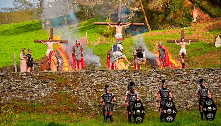 Recreación de la crucifixión en Semana Santa en Asturias. Hombres vestidos de romanos y figuras crucificadas en un paisaje verde.