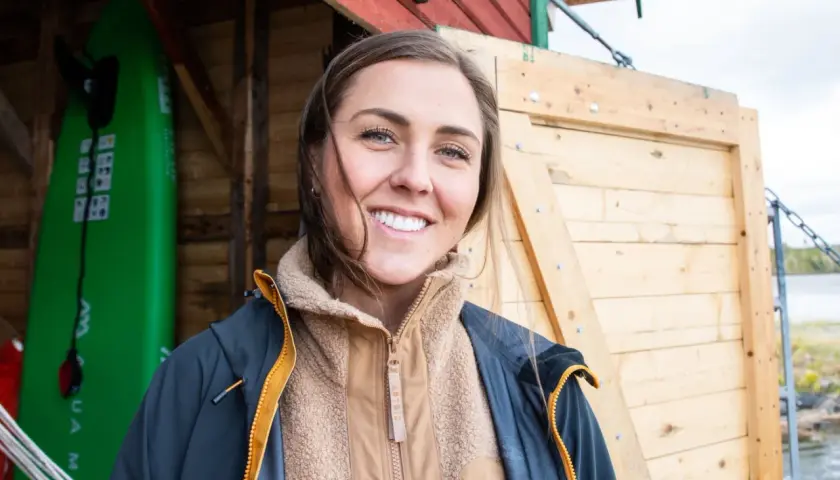 Amanda Robinson ler glatt framför en grön surfbräda och en träbyggnad.