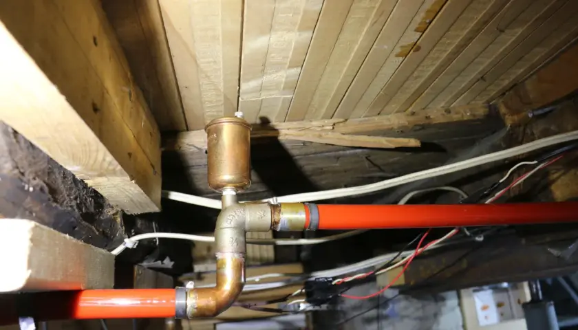 Miedziany odpowietrznik nad czerwonymi rurami, część instalacji, która może pomóc w procesie jak odpowietrzyć bojler ciepłej wody.