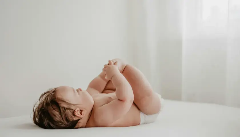 Un neonato con un adorabile culetto rosso, sdraiato su un lettino, gioca con i suoi piedini.
