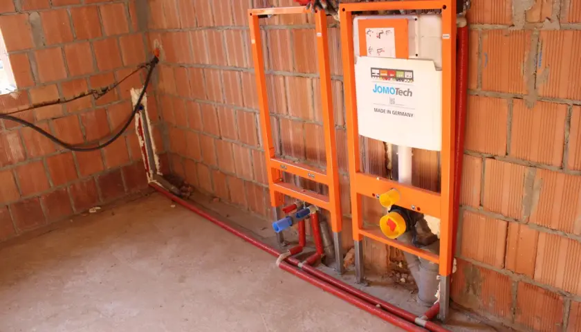 Instalacja hydrauliczna przed tynkami: stelaże podtynkowe, rury i spłuczka JomoTech w budowie.