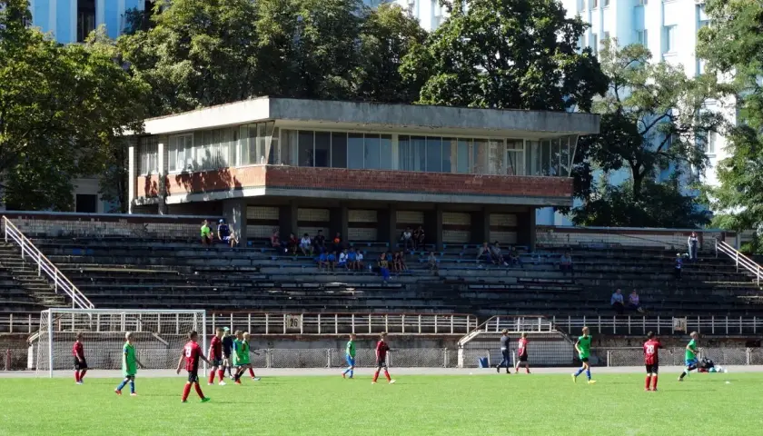 Młodzi piłkarze trenują na boisku. W tle widać trybuny i budynek, część stadionu Dynamo Kijów.