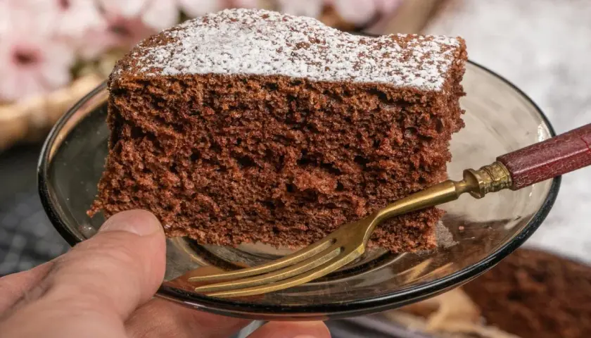 Kawałek najprostszego ciasta czekoladowego, posypana cukrem pudrem, na talerzyku z widelcem.