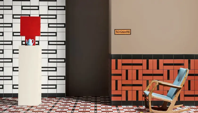 Un soggiorno moderno con pavimenti geometrici. Una poltrona a dondolo blu e legno, un piedistallo con una lampada rossa e una teiera blu.