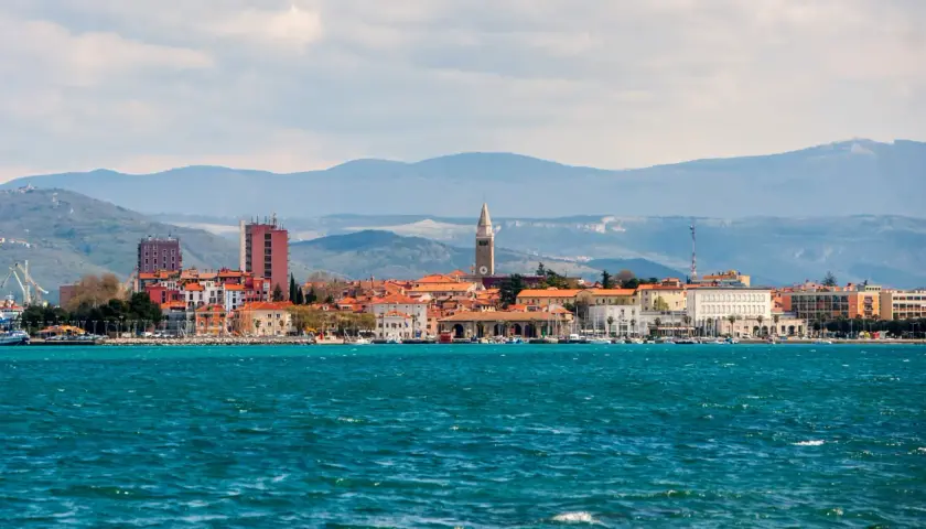 Widok na miasto Koper w Słowenii z turkusowym morzem w tle. W oddali widać góry.