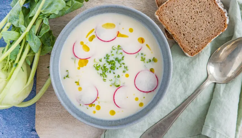 Cremige Kohlrabisuppe low carb, garniert mit Radieschenscheiben und Kresse. Dazu Vollkornbrot und ein Löffel.