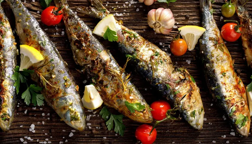 Sardines grillées, citron, tomates cerises et ail sur fond de bois. Faut-il vider les sardines avant de les cuire ?