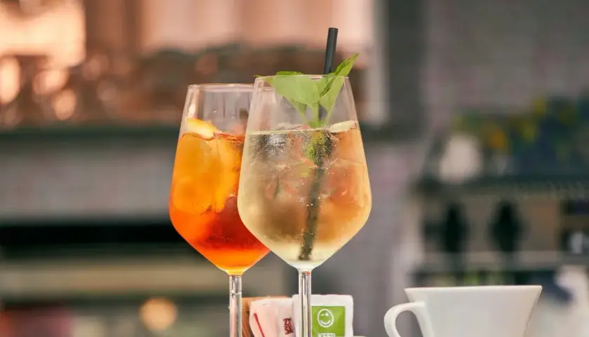 Dwa orzeźwiające drinki, jeden pomarańczowy z plasterkiem cytryny, drugi jasny z miętą i słomką. Idealne na letnie popołudnie.