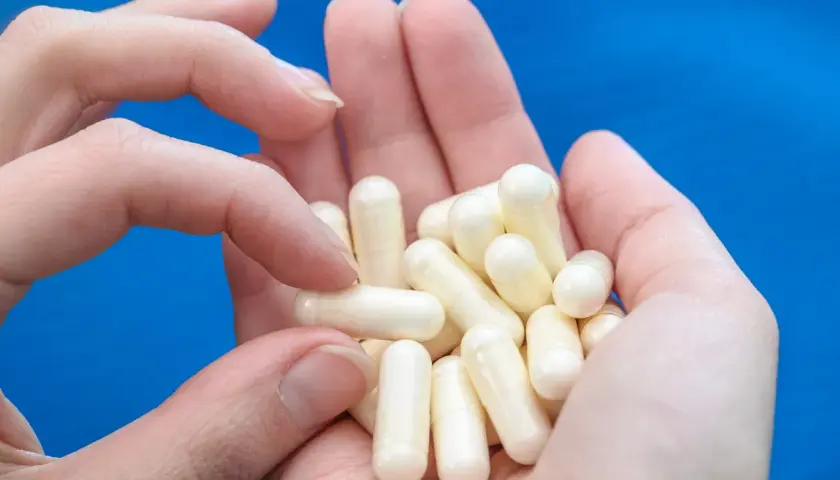 Dłonie trzymają garść białych kapsułek, które mogą zawierać biotynę, wspierającą zdrowie włosów i paznokci.