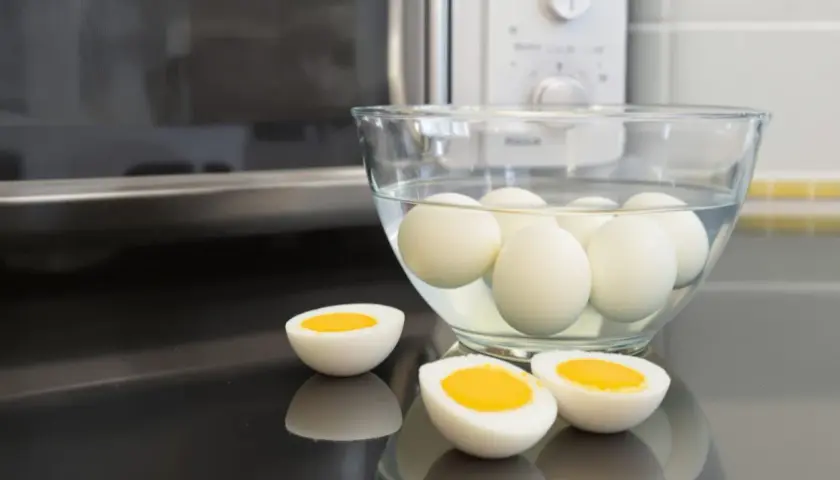 Des œufs durs dans un bol d'eau, prêts à être dégustés. Un œuf est coupé en deux, révélant un jaune d'or parfait. La méthode de cuisson par oeuf dur micro onde est rapide et facile.