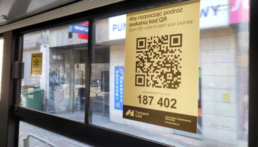 W autobusie widoczny jest żółty plakat z kodem QR i napisem "Aby rozpocząć podróż zeskanuj kod QR". Pod kodem znajduje się numer 187 402.